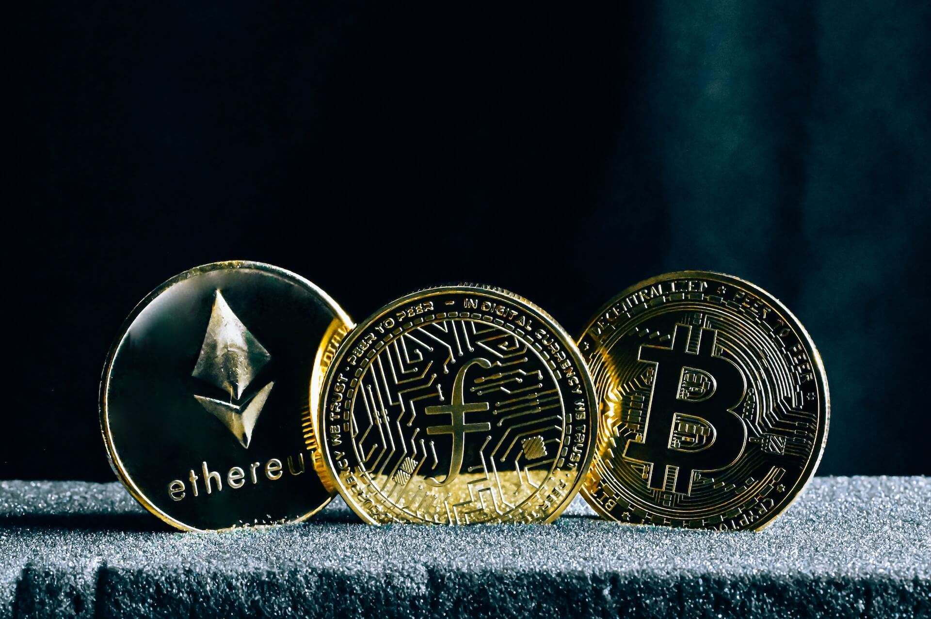 Bitcoin, Ethereum, and Filecoin physical coins representing different cryptocurrencies.