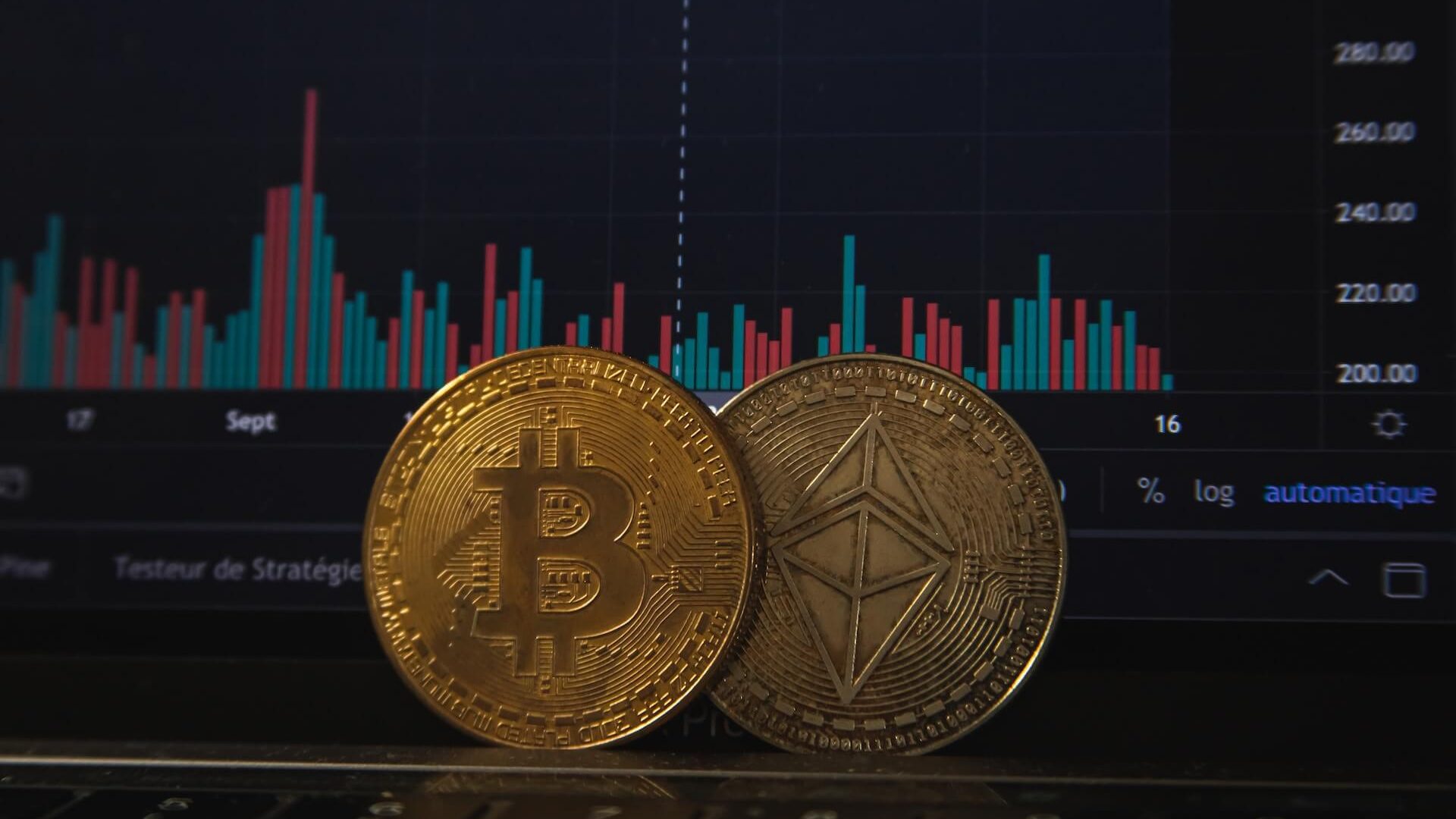 Physical Bitcoin and Ethereum coins with a computer screen showing cryptocurrency market data.